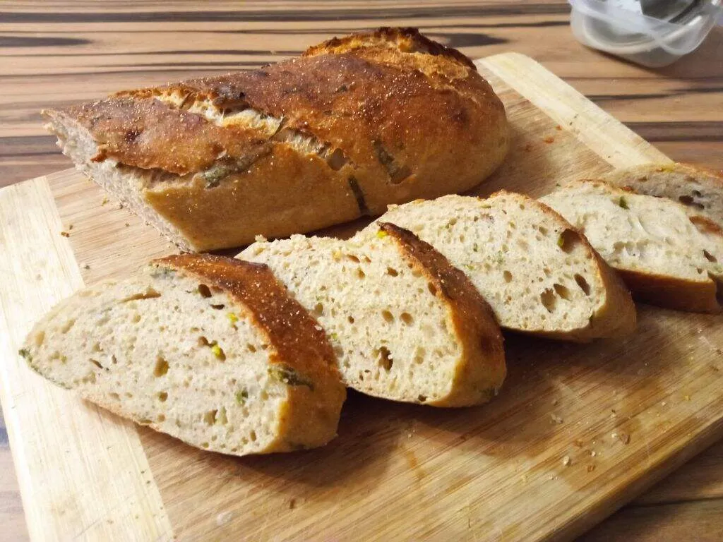 Szeletelt francia kenyér egy deszkán kínálva, egyenletes bélzet és belesütött illatozó medvehagyma