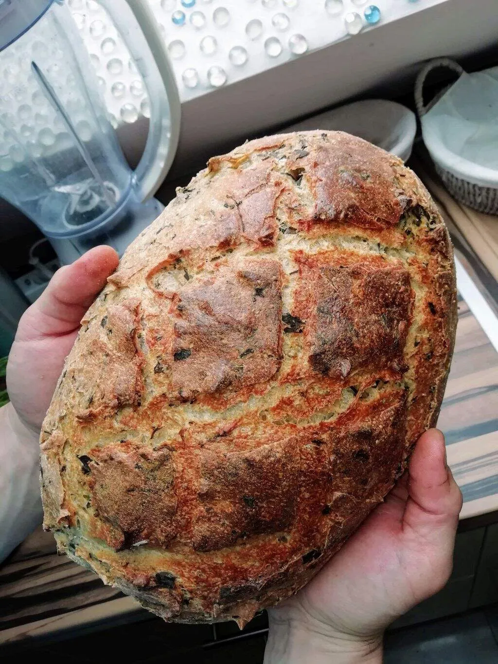 Egy kézben tartott kenyér, melyen jól látszik a belesütött, illatozó bazsalikom